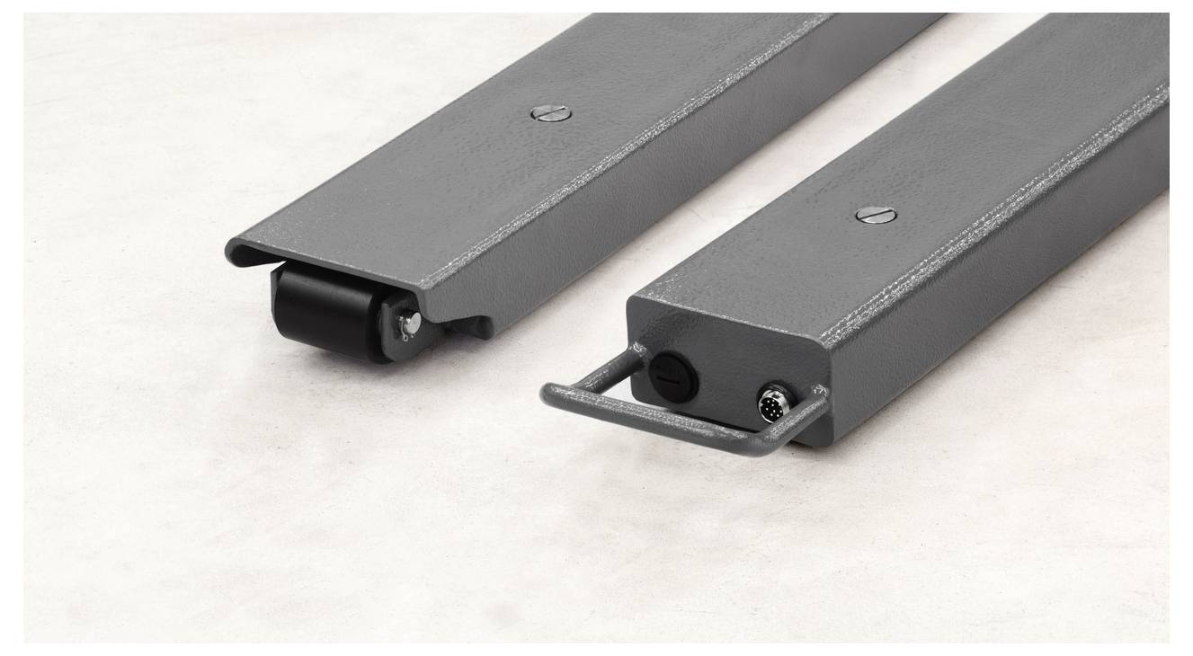 Two grey metal parts with flanges and rolls at one end are lying on a light surface. One has a square cross-section, the other is round.