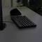A black wireless keyboard and a mouse are lying on a dark table next to a monitor.