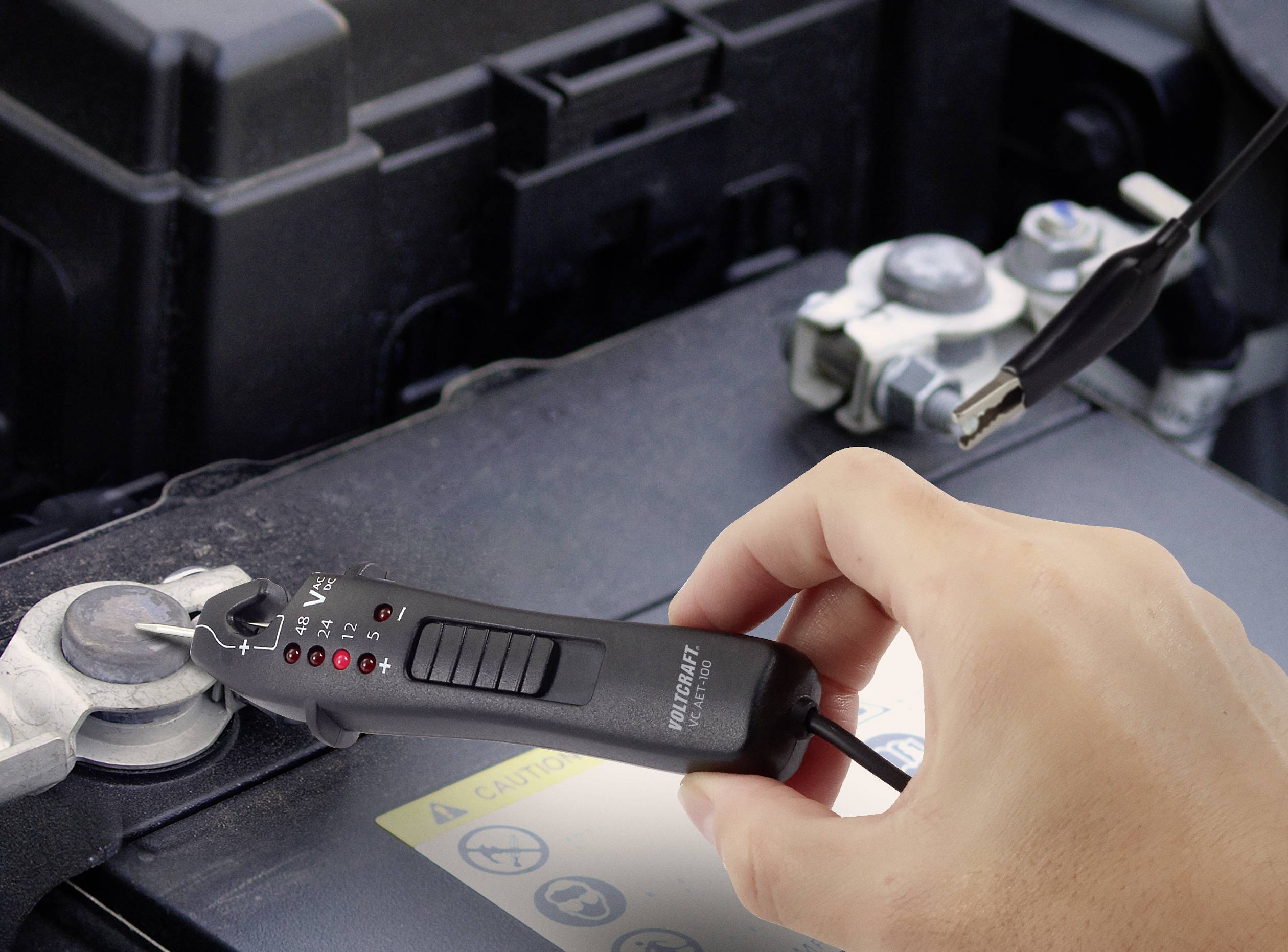 A hand is using a multimeter to check the voltage of a car battery.