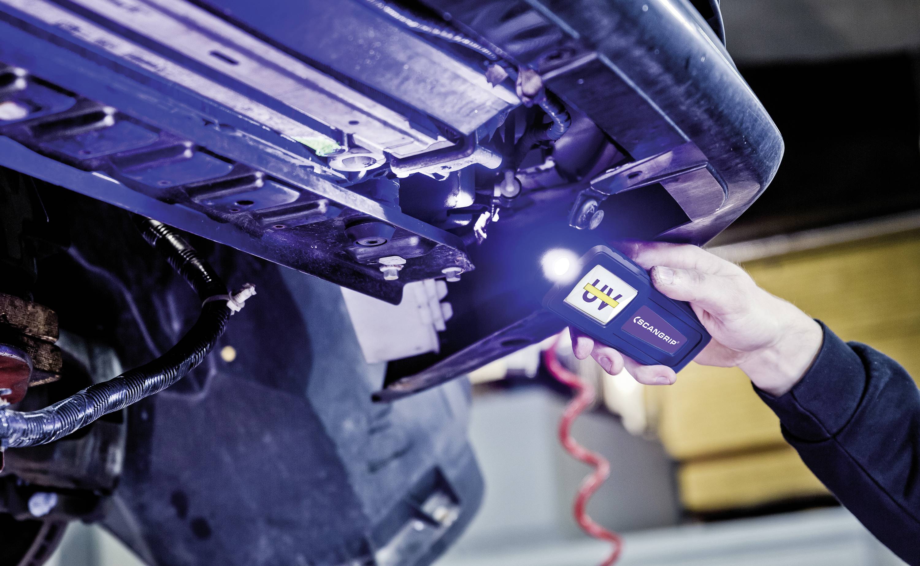 A person is inspecting the underside of a vehicle with a torch in a workshop environment.