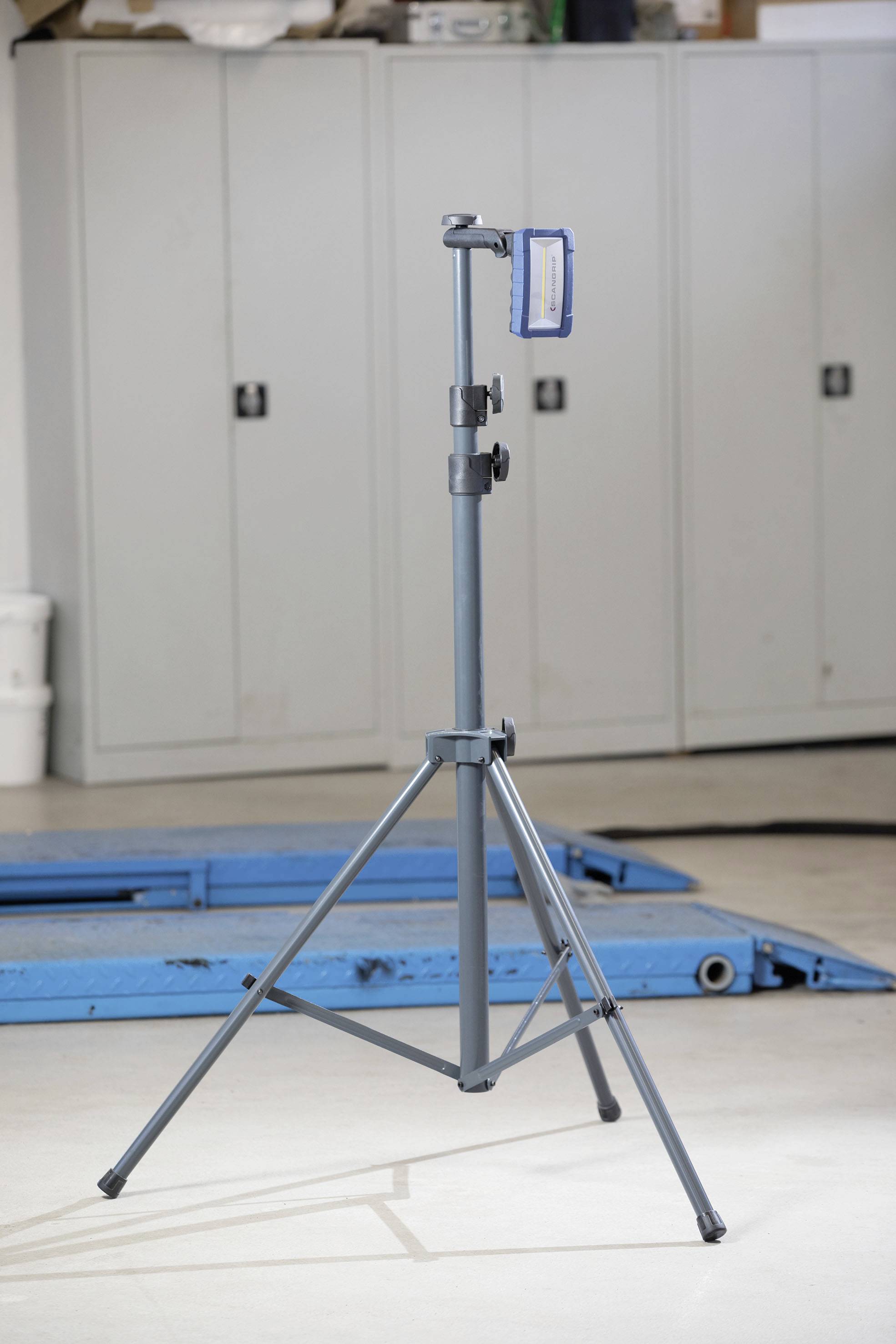 A blue, folded camera tripod stands in a room with grey cupboards in the background.