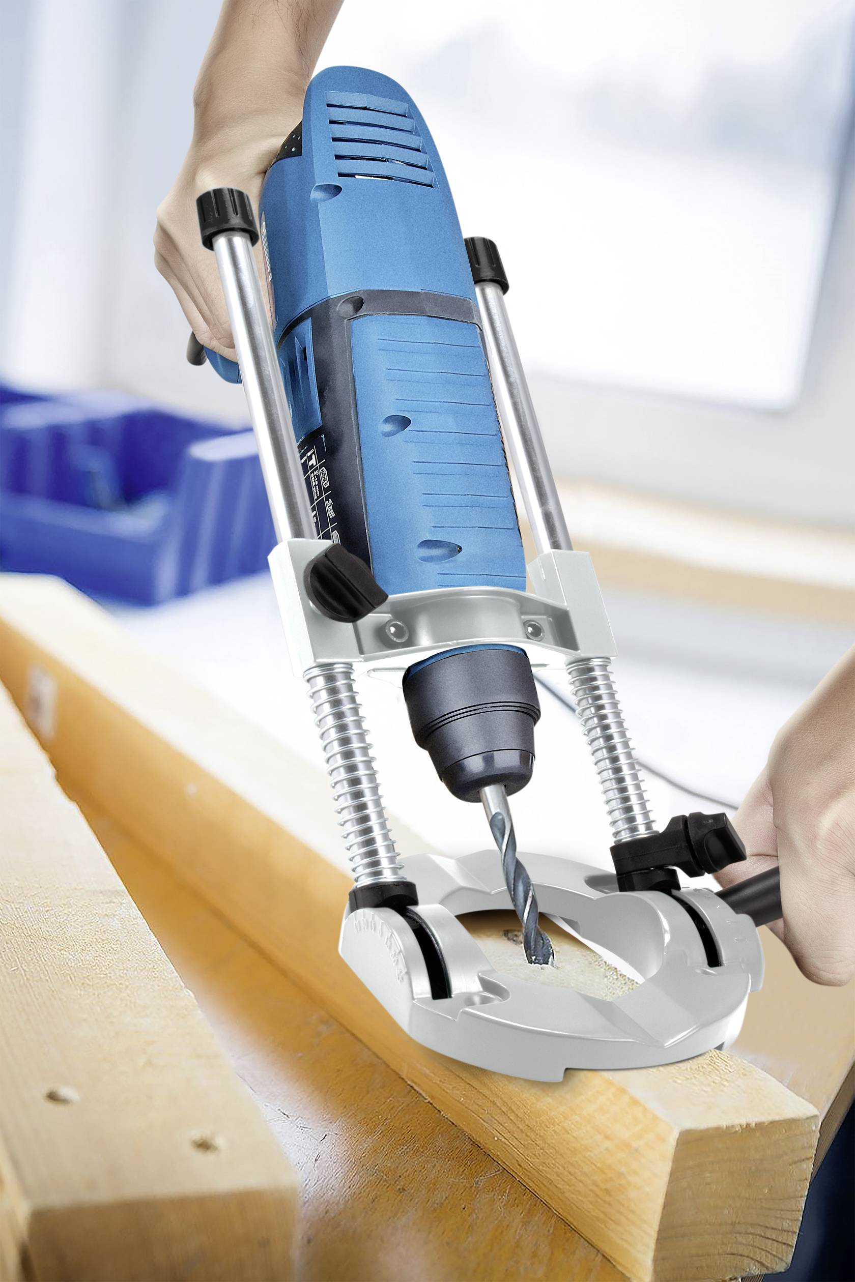 A person is drilling a hole in a wooden board using a blue drill on a workbench.