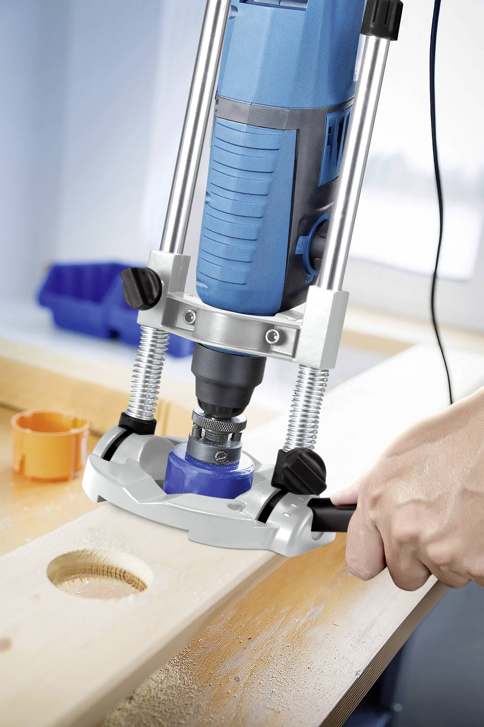 A hand holds an electric router that is precisely milling a circular hole in a wooden board.