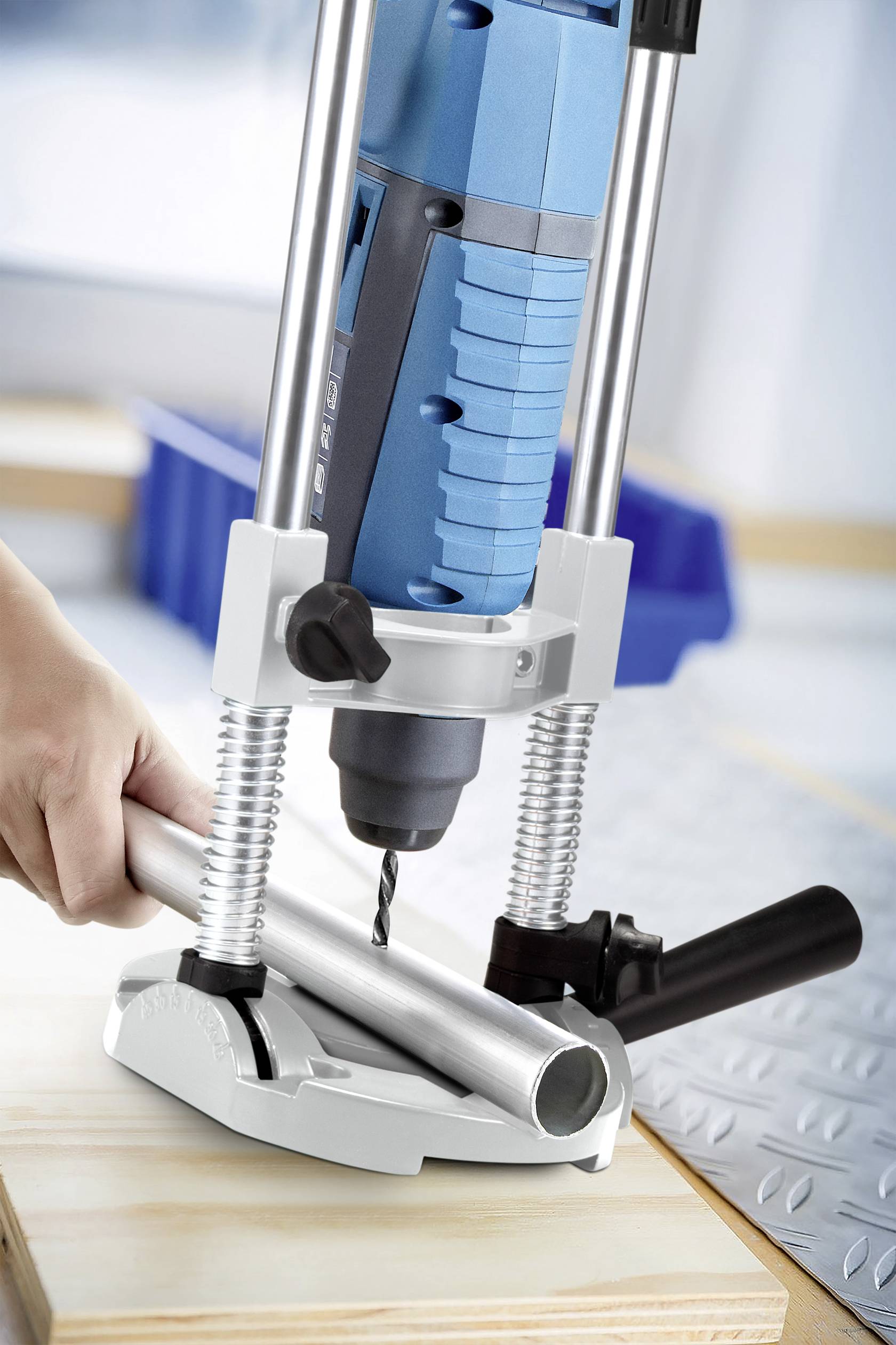 A drill with a stand is holding a metal pipe on a wooden base, with a drill bit positioned on it.