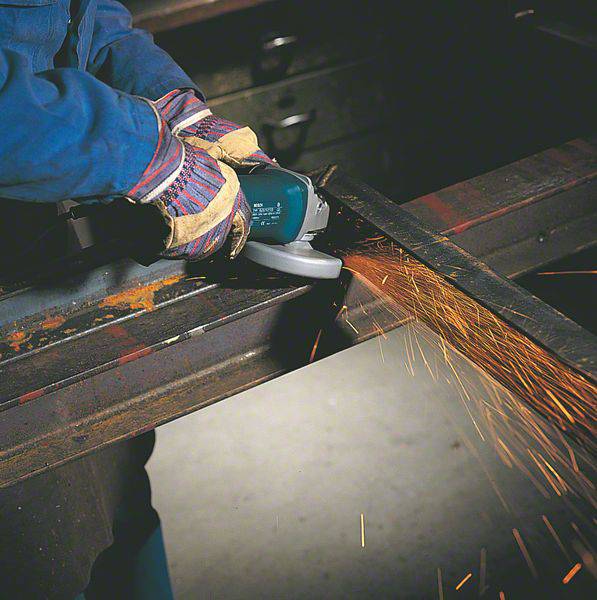 A person is grinding metal with an electric grinding machine, while sparks are flying. They are wearing protective clothing and gloves.