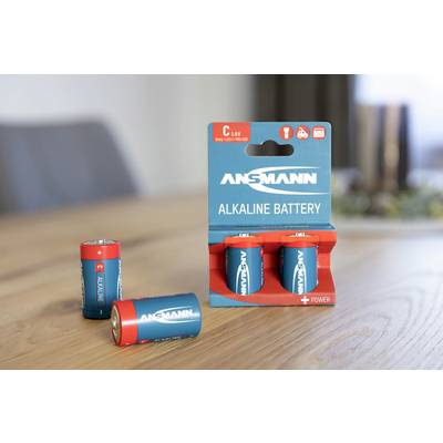 Three Ansmann C batteries on a table, two loose and one in its packaging. Room in the background slightly out of focus.