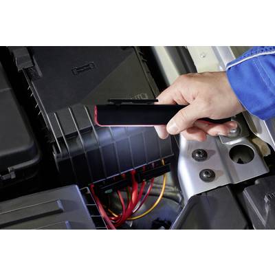 A person is holding a lamp and shining light onto an open engine bay with visible cables and battery cover.