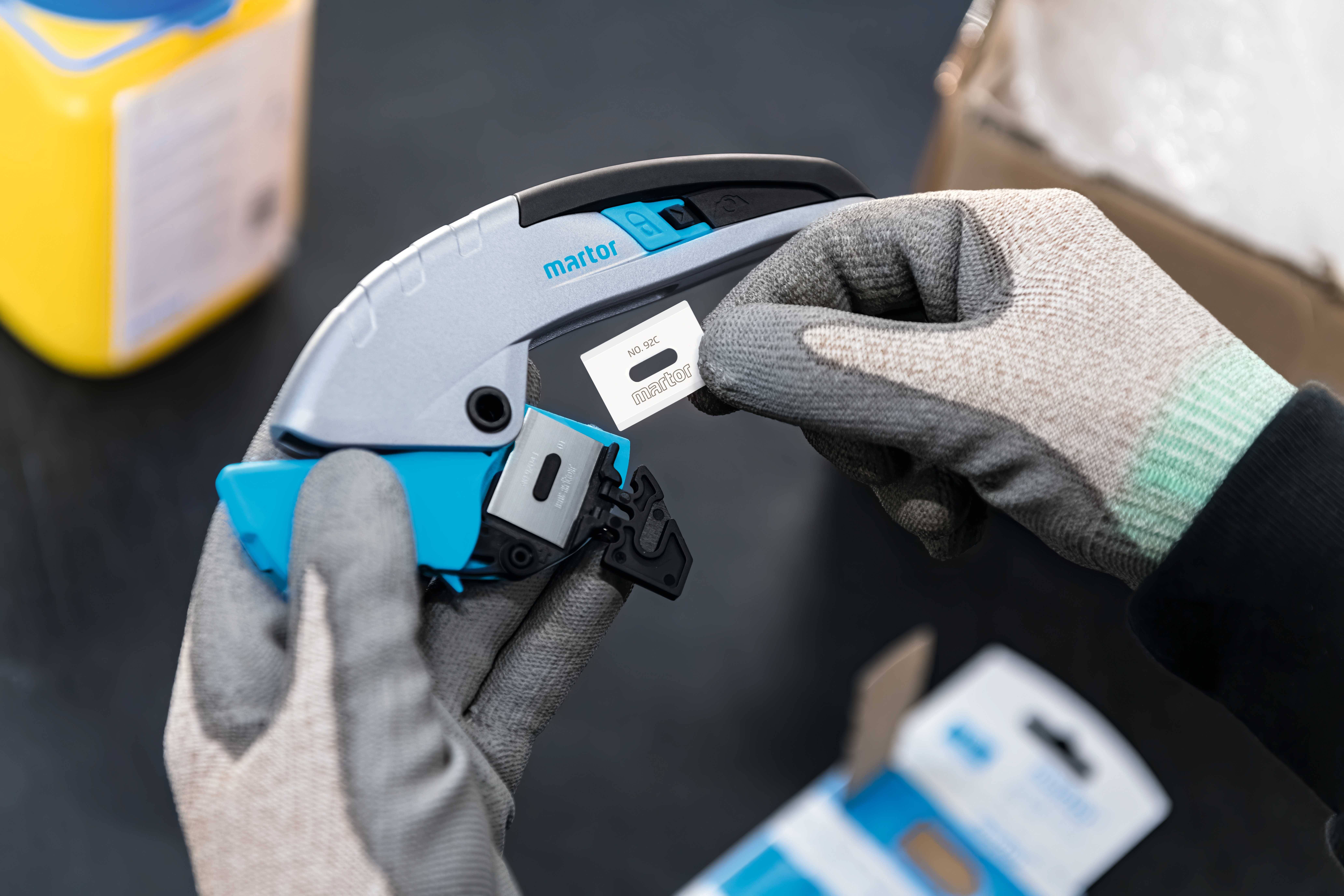 A person wearing gloves is holding a grey and blue device and placing a small white label with black text on it.