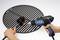 A person is cleaning a barbecue grill with a brush and a blue hot air blower.