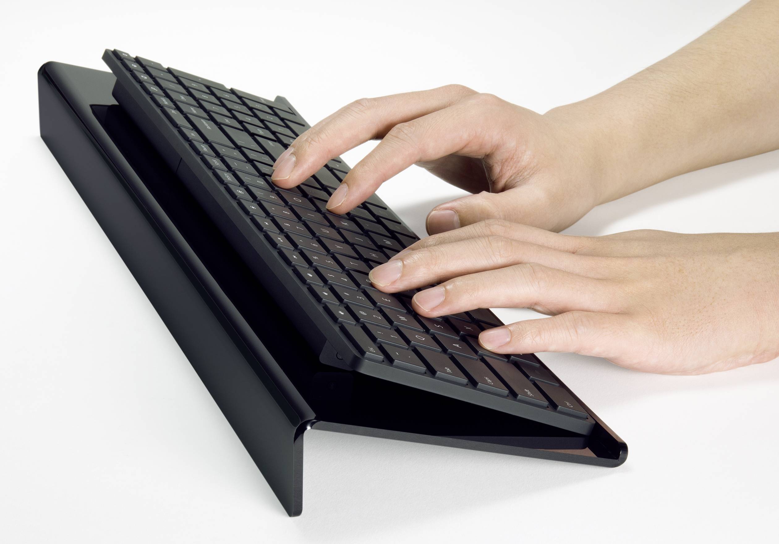 Hands typing on a black keyboard, which is resting on an angled, modern stand.