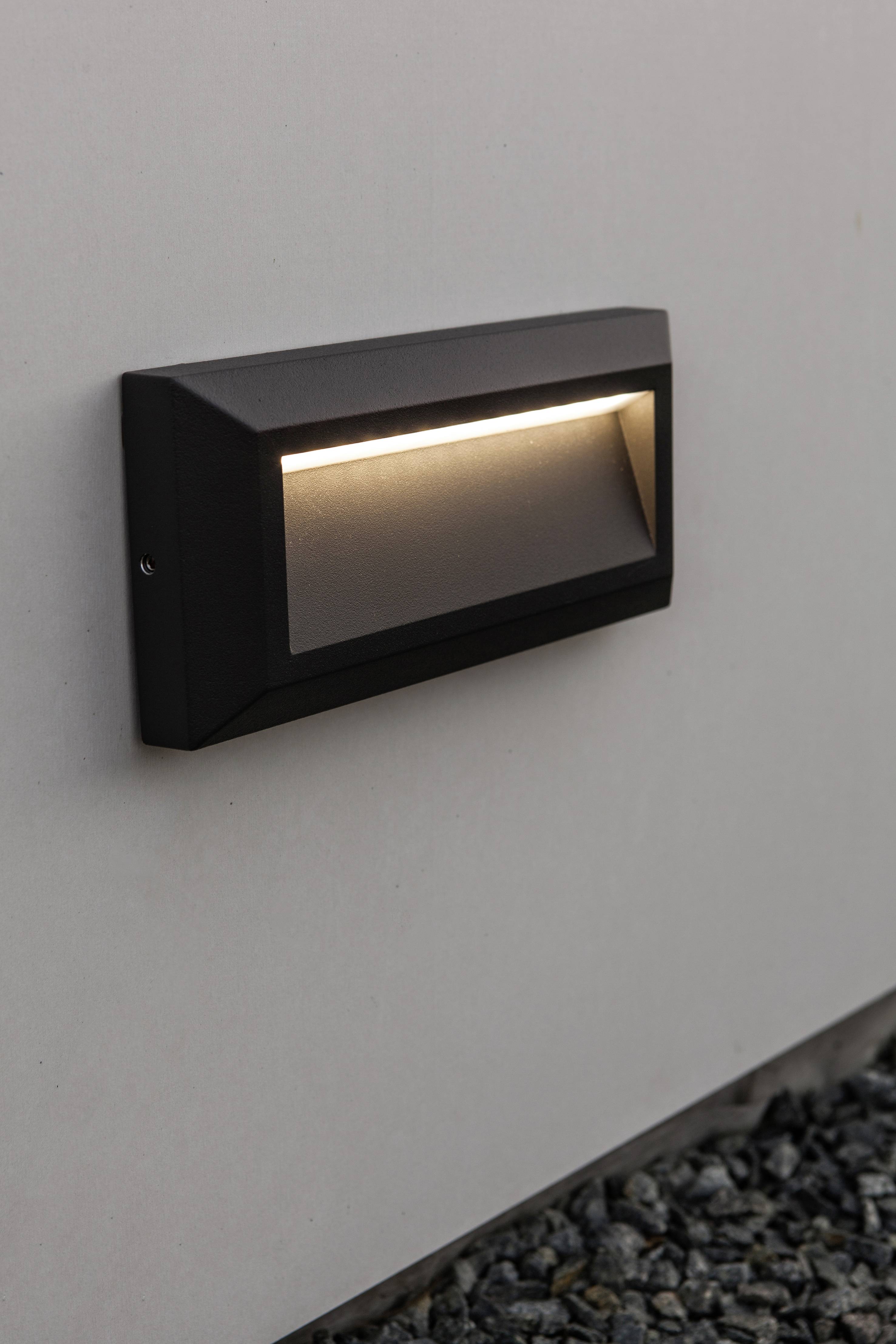 A modern, rectangular LED wall light with a black housing is mounted on a light-coloured wall, illuminating downwards.