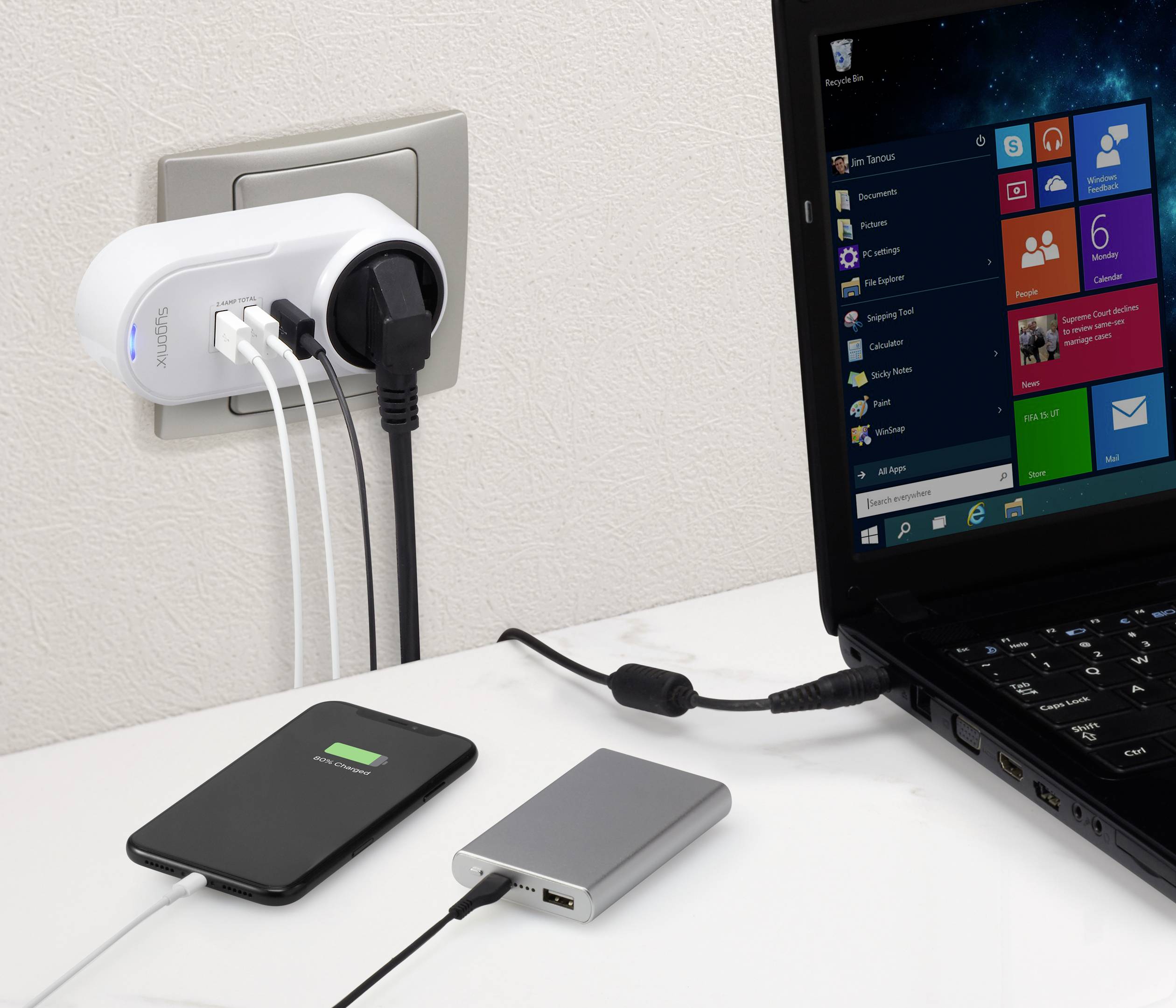 A laptop is plugged into a power socket. Two mobile devices are charging via USB ports on a multi-socket adaptor.