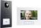 A video doorbell displays the image of a smiling woman on the monitor. The system consists of a camera and a screen.