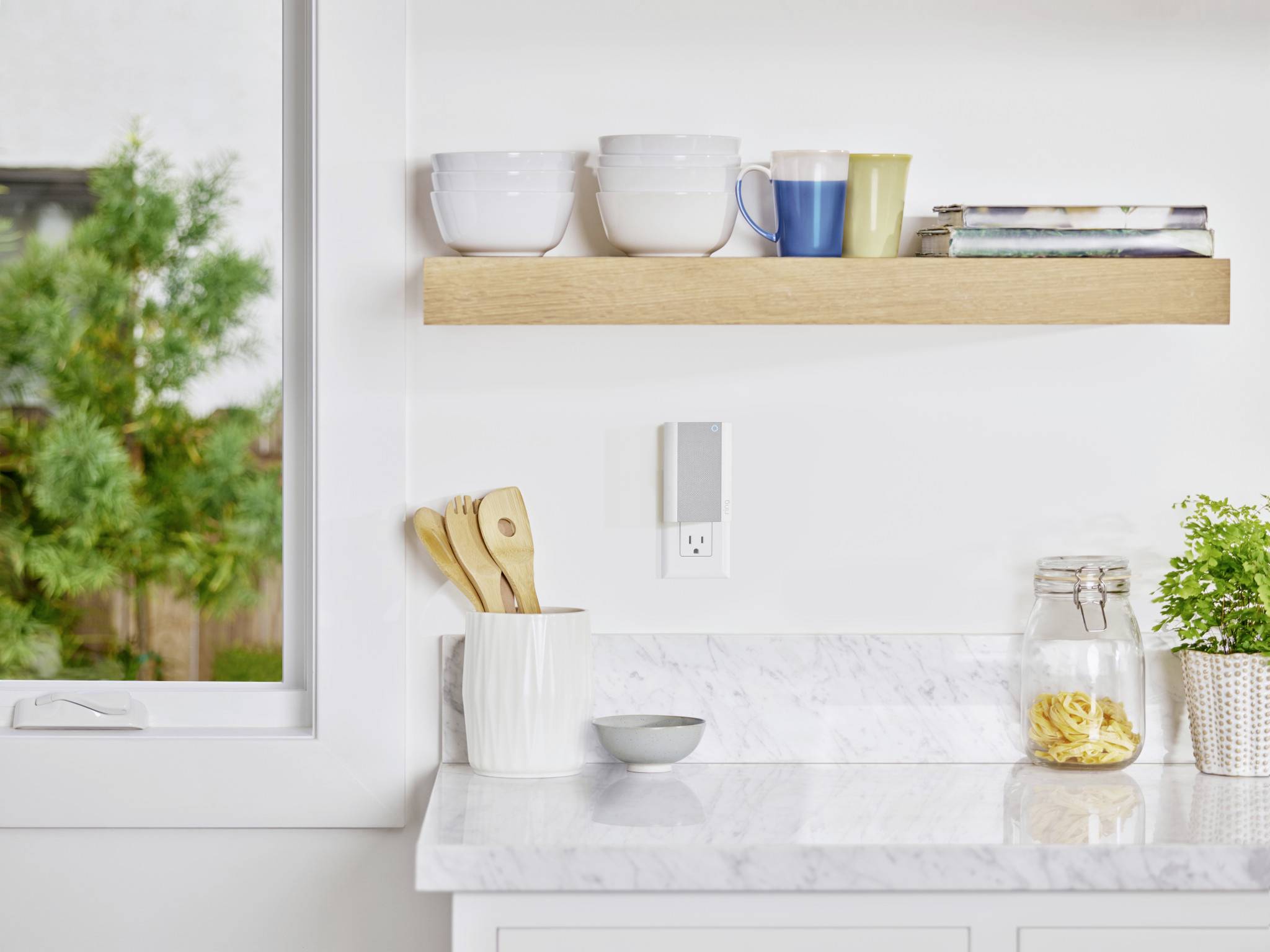 Bright, modern kitchen with white walls and a marble worktop. On the shelf are mugs, books and a small plant.