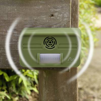 A green ultrasonic animal deterrent device, mounted on a wooden post in the garden, emits sound waves to deter wildlife.