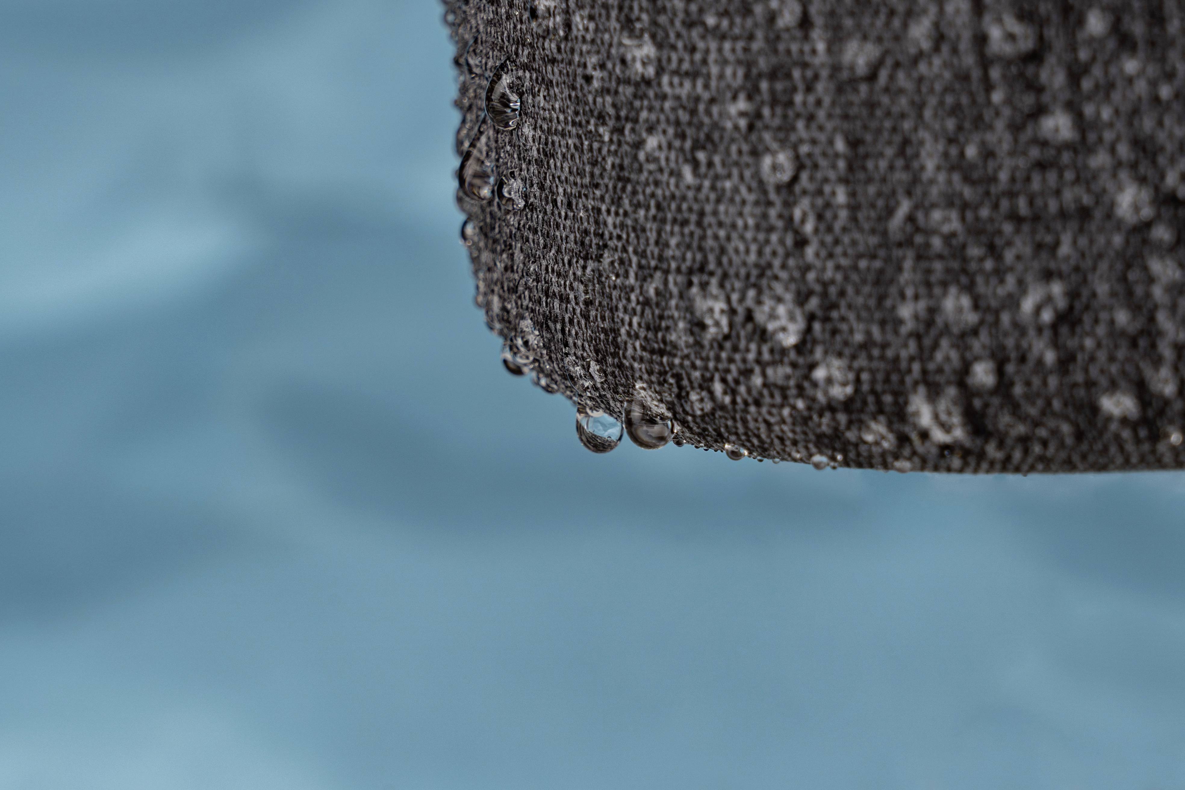 Water droplets fall from a wet, grey fabric, with a blurred blue background in front.