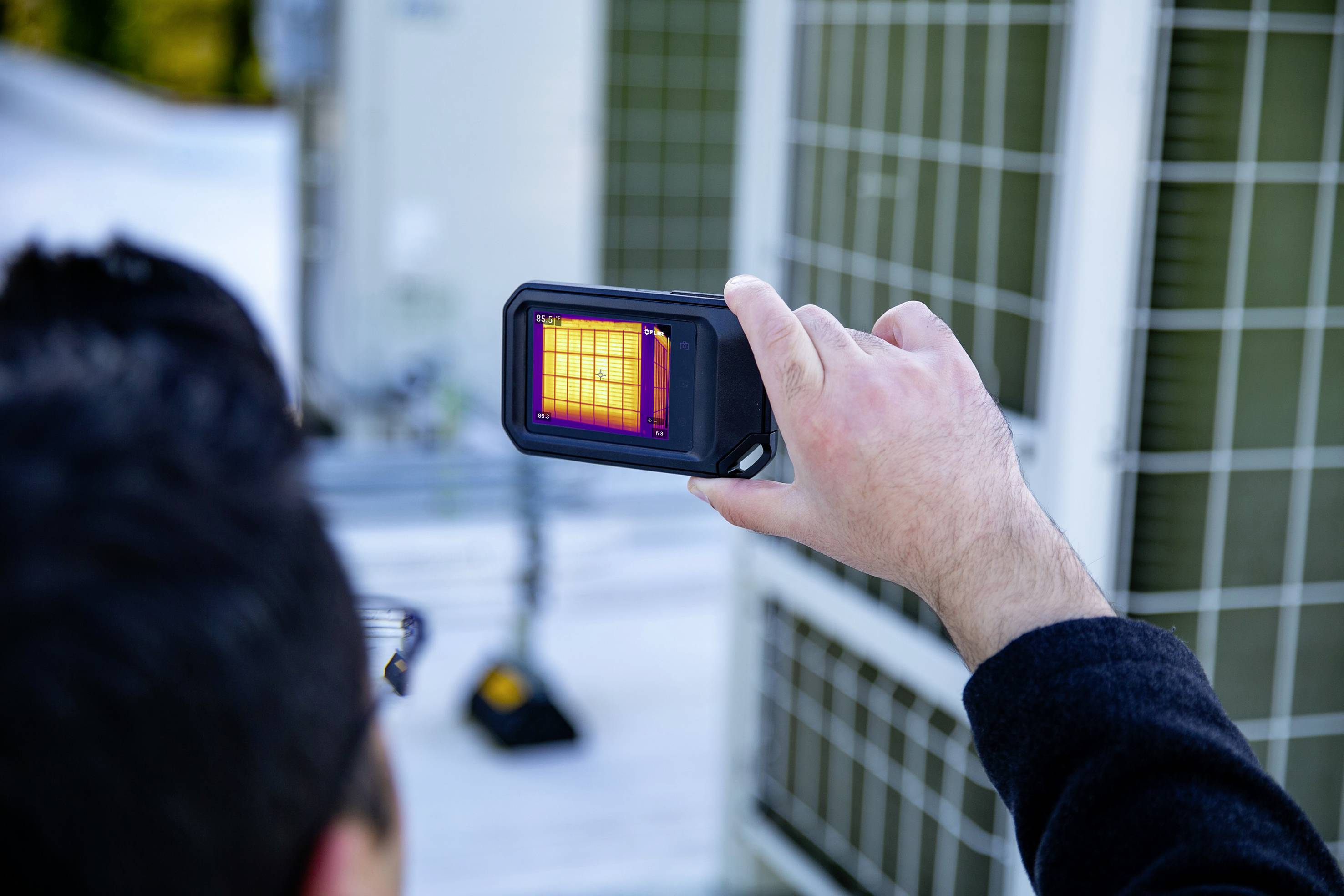 A person is holding a device that displays the thermal radiation of an object. The screen shows a thermal image in various colour tones.