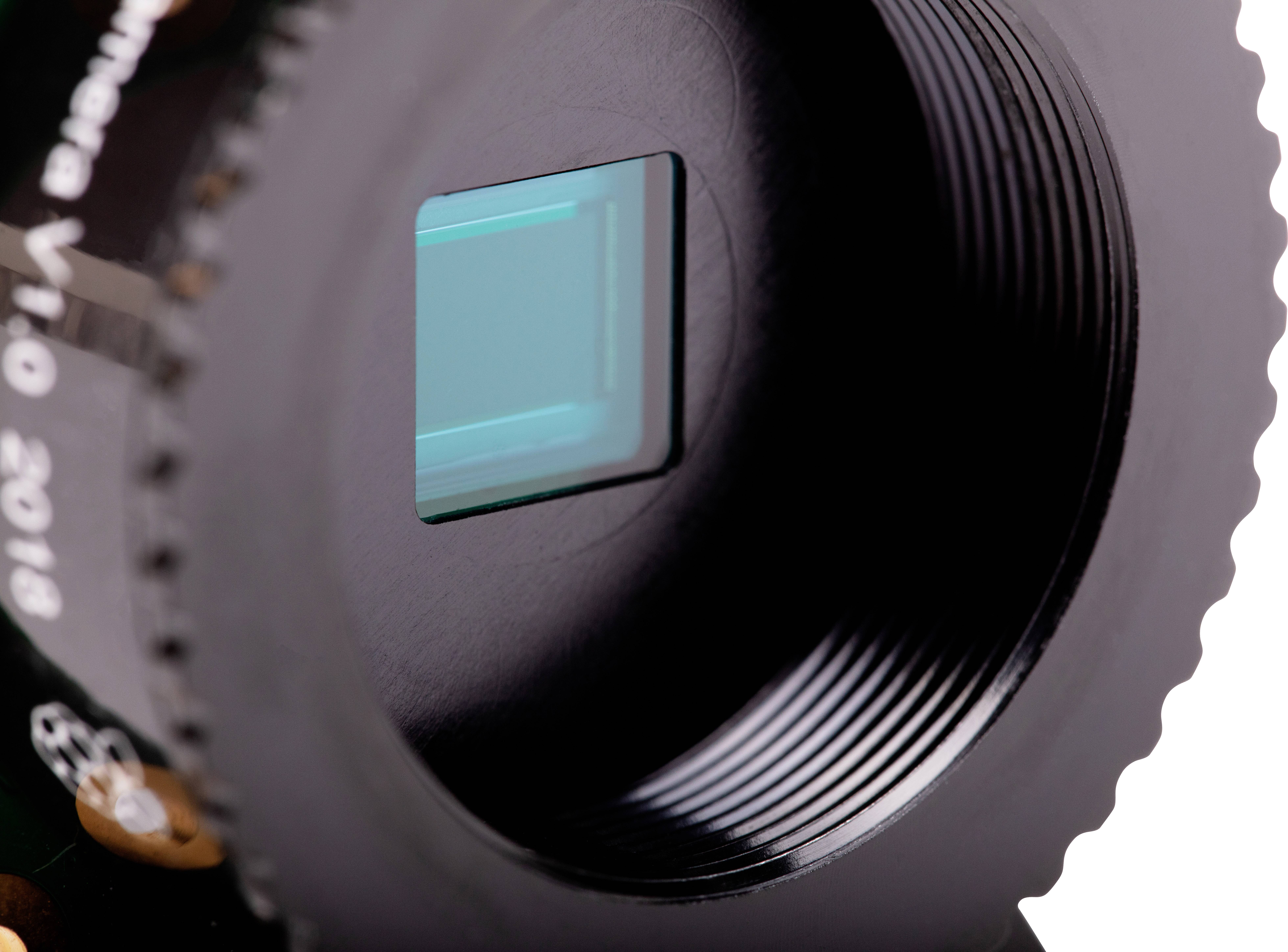 Close-up of a camera lens with the image sensor visible inside. Subtle details and structures of the lens are discernible.