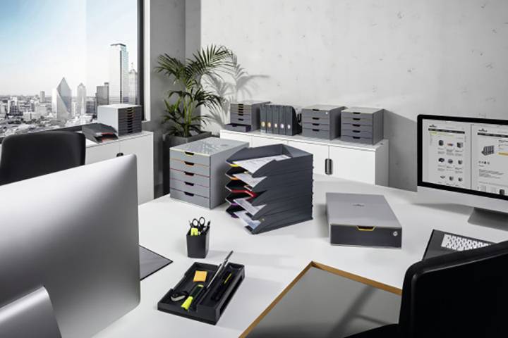 A modern office with a city view. Computer screens, filing trays, and office supplies are placed on the desk.