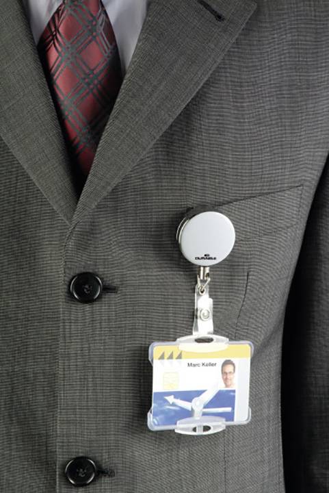 A person is wearing a grey suit with a red tie, wearing an ID card on a clip attached to the suit jacket pocket.