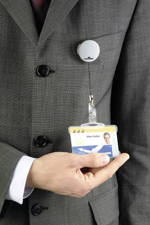 A person in a suit is holding a name badge in their hand. The badge is attached with a clip to the lapel.