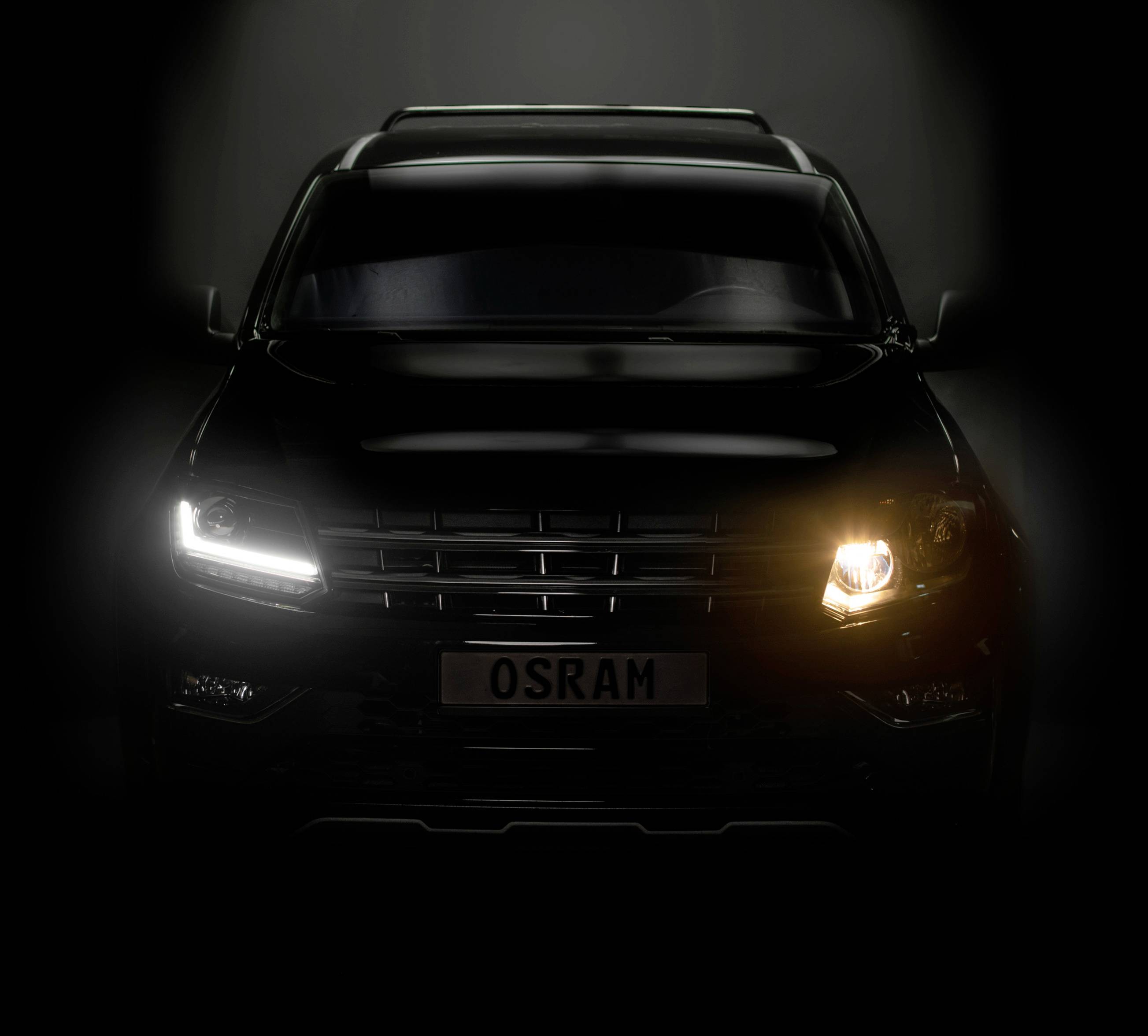 A car with one headlight gleaming in white light, the other in warm yellow. Number plate reads 'OSRAM'.