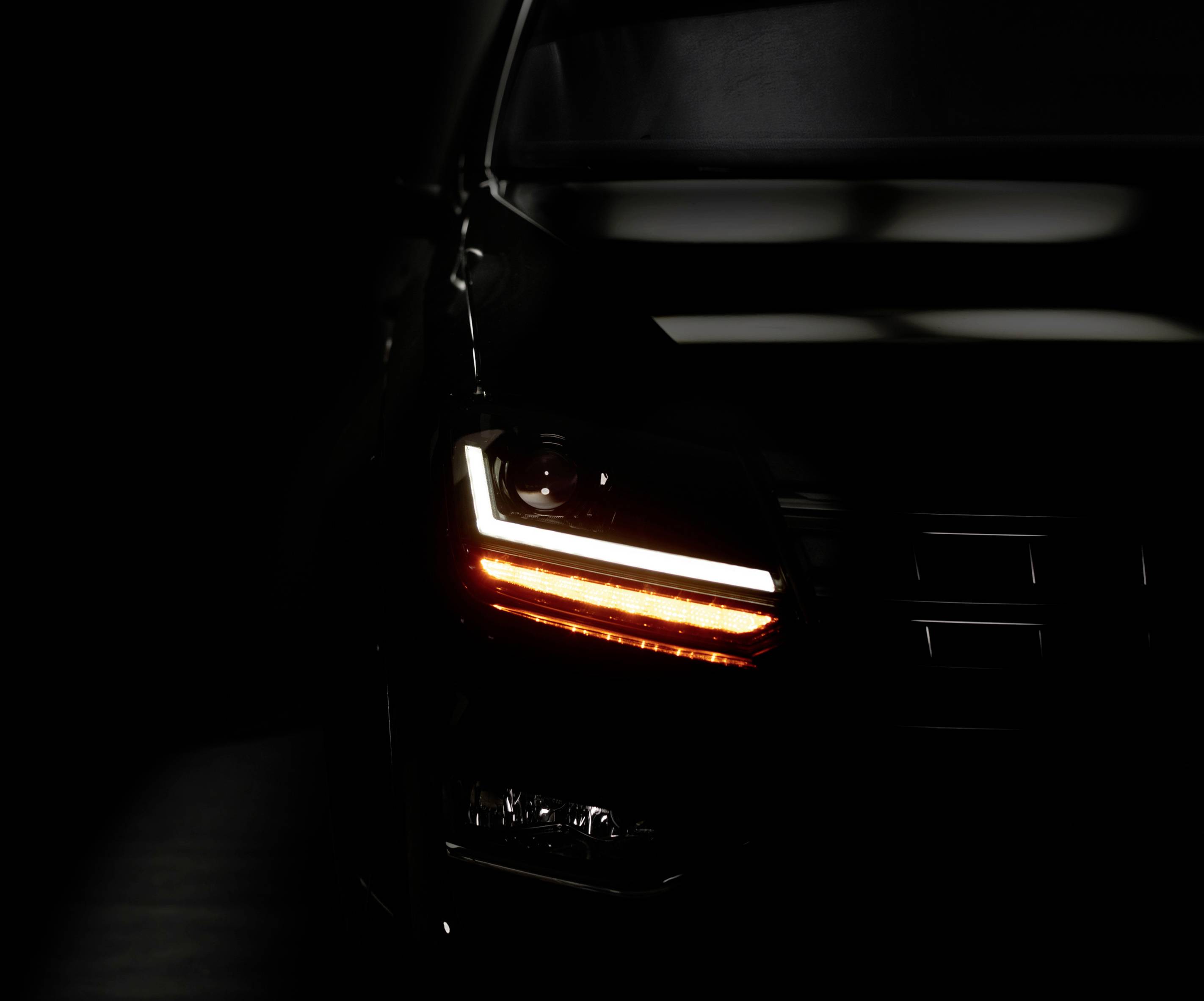A car with its right headlight and rear light switched on, against a dark background for a dramatic effect.