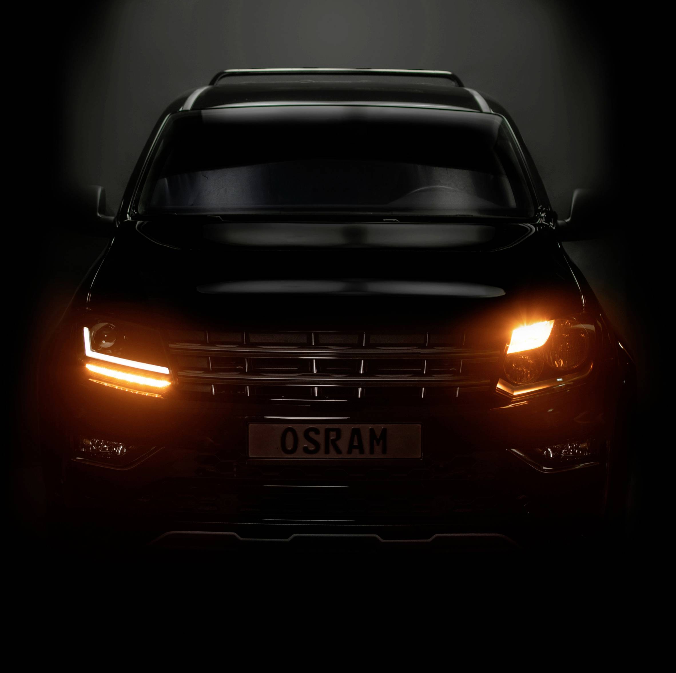 A black car with an illuminated indicator light, captured head-on, displaying the number plate 'OSRAM' in a dark environment.
