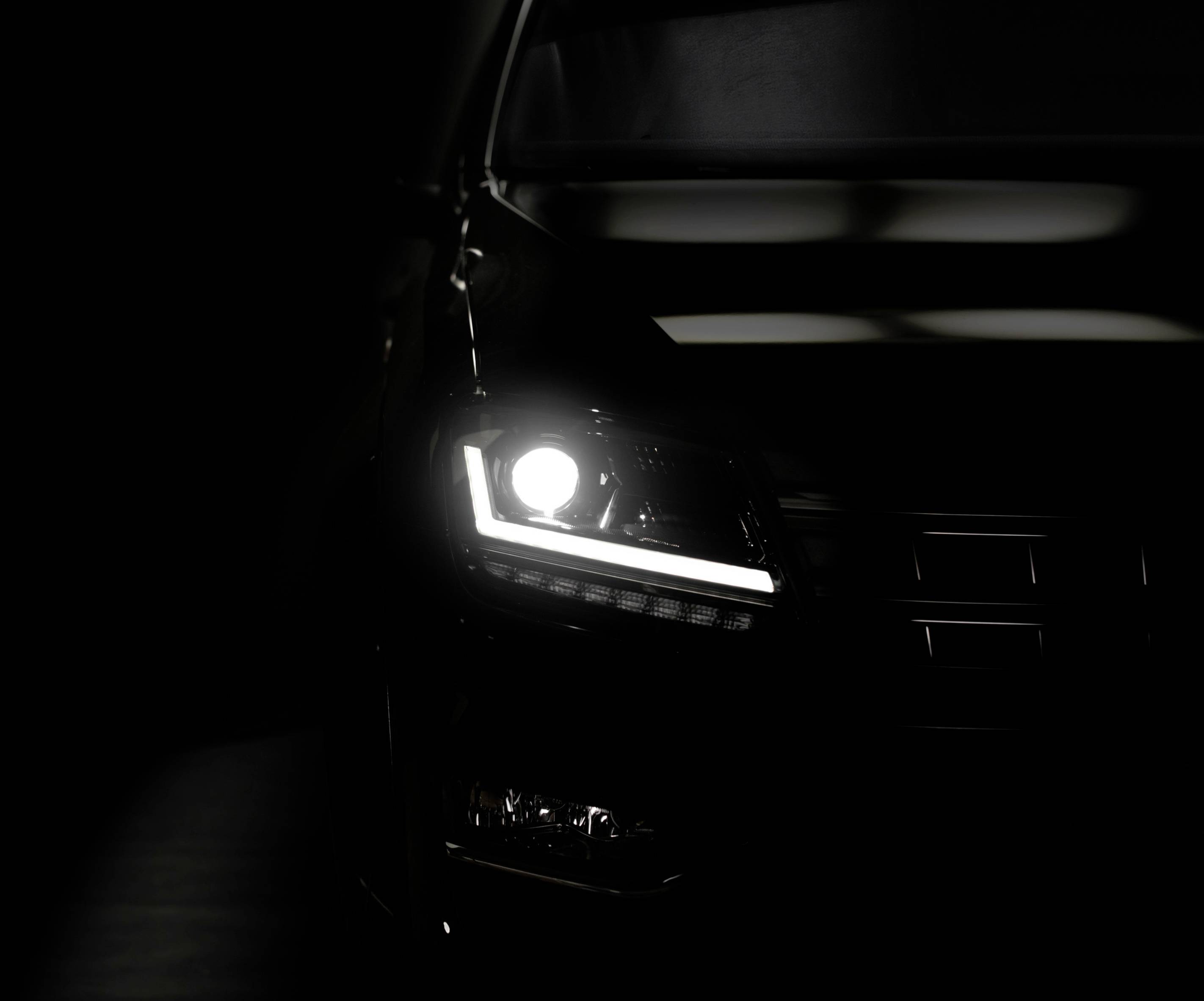 A car headlight shines brightly in a dark environment. Only part of the vehicle's front is visible.