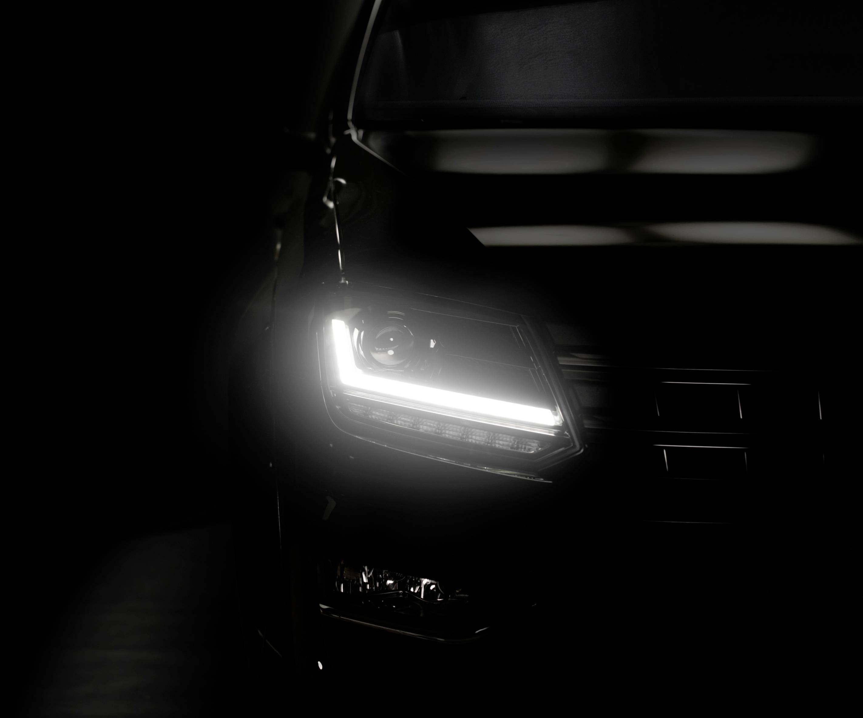 The image shows the glowing headlight of a car in the darkness, which is only partially visible and illuminates the foreground.