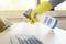A person is cleaning a computer keyboard with a disinfectant spray while wearing yellow rubber gloves.