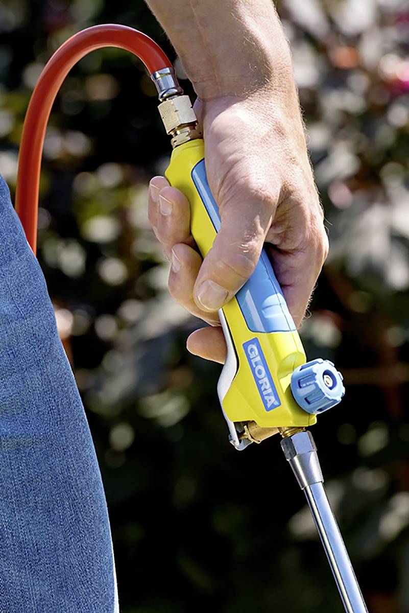 A hand is holding a yellow and blue gas burner with a red hose outdoors.