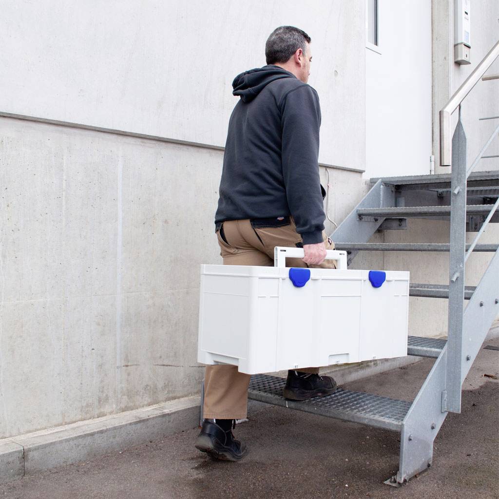 A person is carrying a white toolbox up the stairs to a door.
