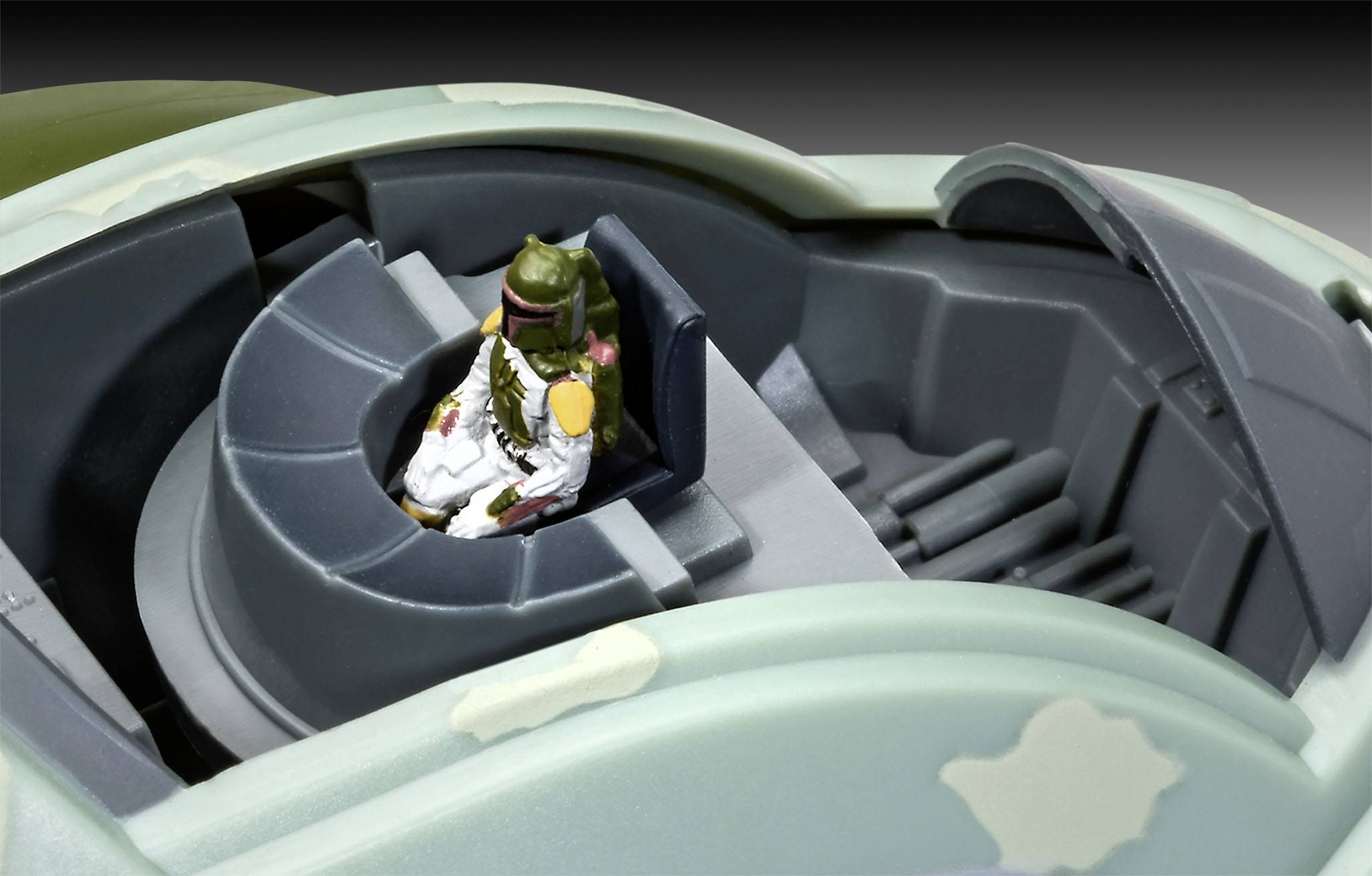 Toy figure of a green bounty hunter with a helmet, sitting in a grey cockpit spacecraft.