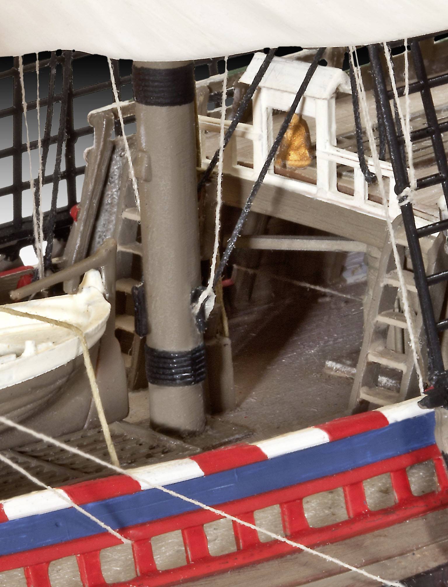 Model of a sailing ship's deck with a lifeboat, masts, and rigging. In the background, a wheelhouse with an illuminated window.