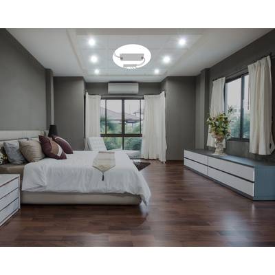 A contemporary bedroom with wooden flooring. A large bed with white sheets stands on the left, with bedside tables beside it. Large windows with curtains provide daylight. A low sideboard is positioned on the right.