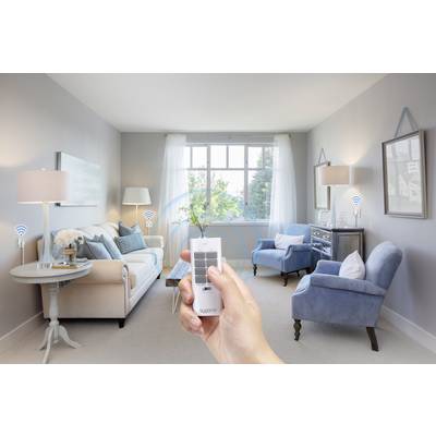 A hand is holding a remote control in a living room with two armchairs, a sofa, and lamps. Wireless symbols indicate smart home functions.