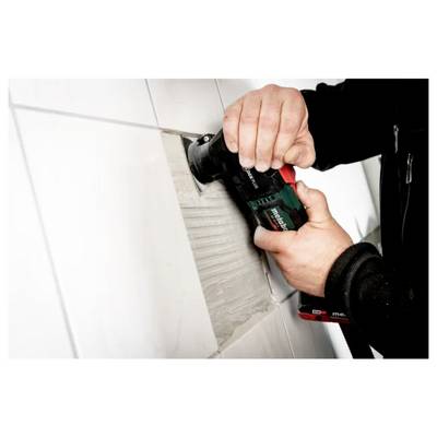A person uses a power tool to remove a tile from a wall, focusing on precision as they work between the tiles.