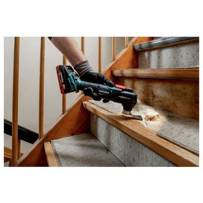 A person uses an electric power tool to sand wooden stairs, smoothing the surface. The tool is black and teal, operated with one hand.