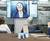 A group of people in a conference room participating in a video conference with a woman on a large screen.