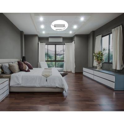 A modern bedroom with wooden flooring, large windows, a bed dressed in white bedding and white curtains. A plant pot sits on the chest of drawers.