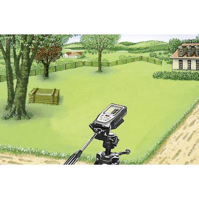 A surveying instrument stands on a tripod in a rural landscape with trees, a house and a fence in the background.