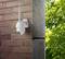Security camera mounted on a brick wall, with green trees in the background.
