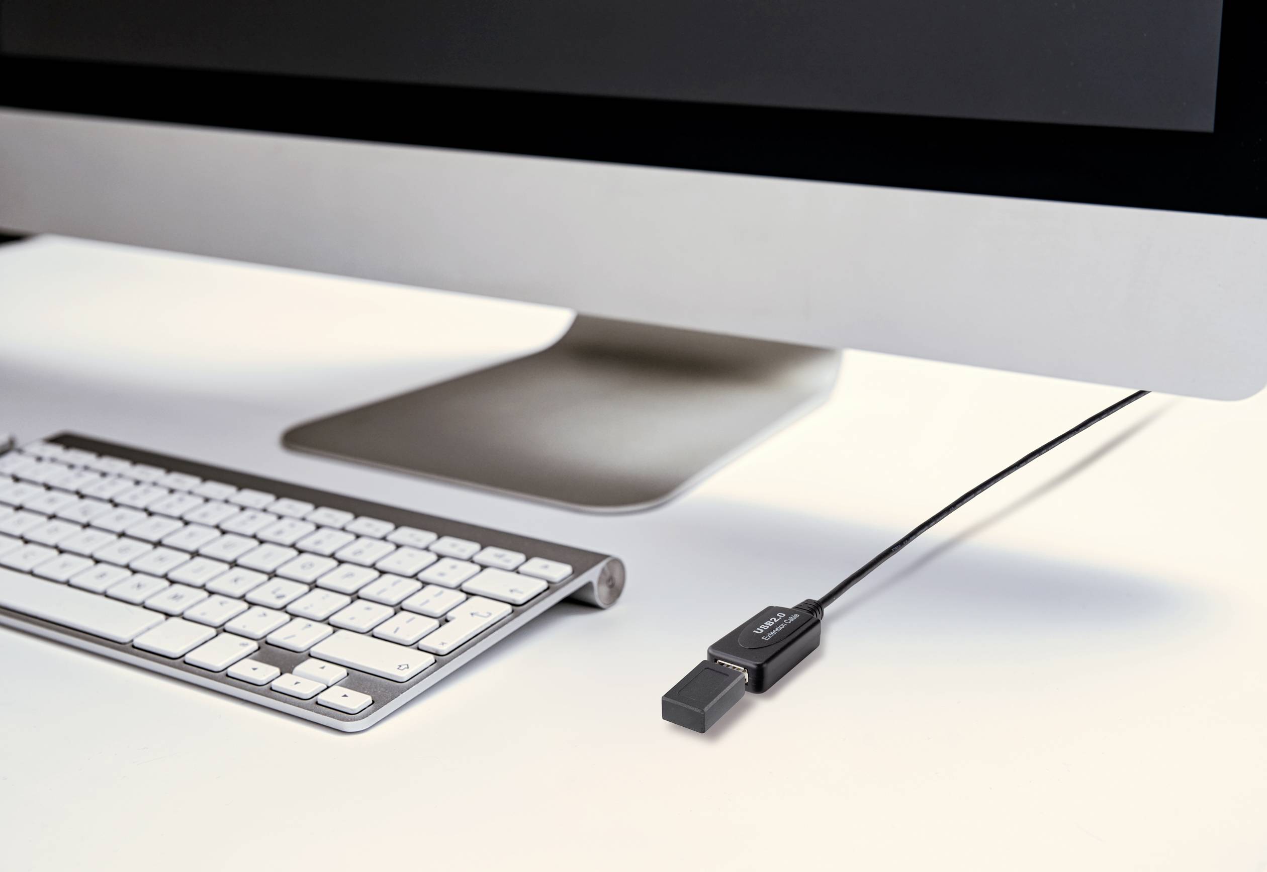 A computer screen with a keyboard and a connected USB stick are lying on a white table.