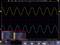 'Oscilloscope screen shows two waveforms: yellow above, blue below. Time and frequency measurements on the bottom left are highlighted.'