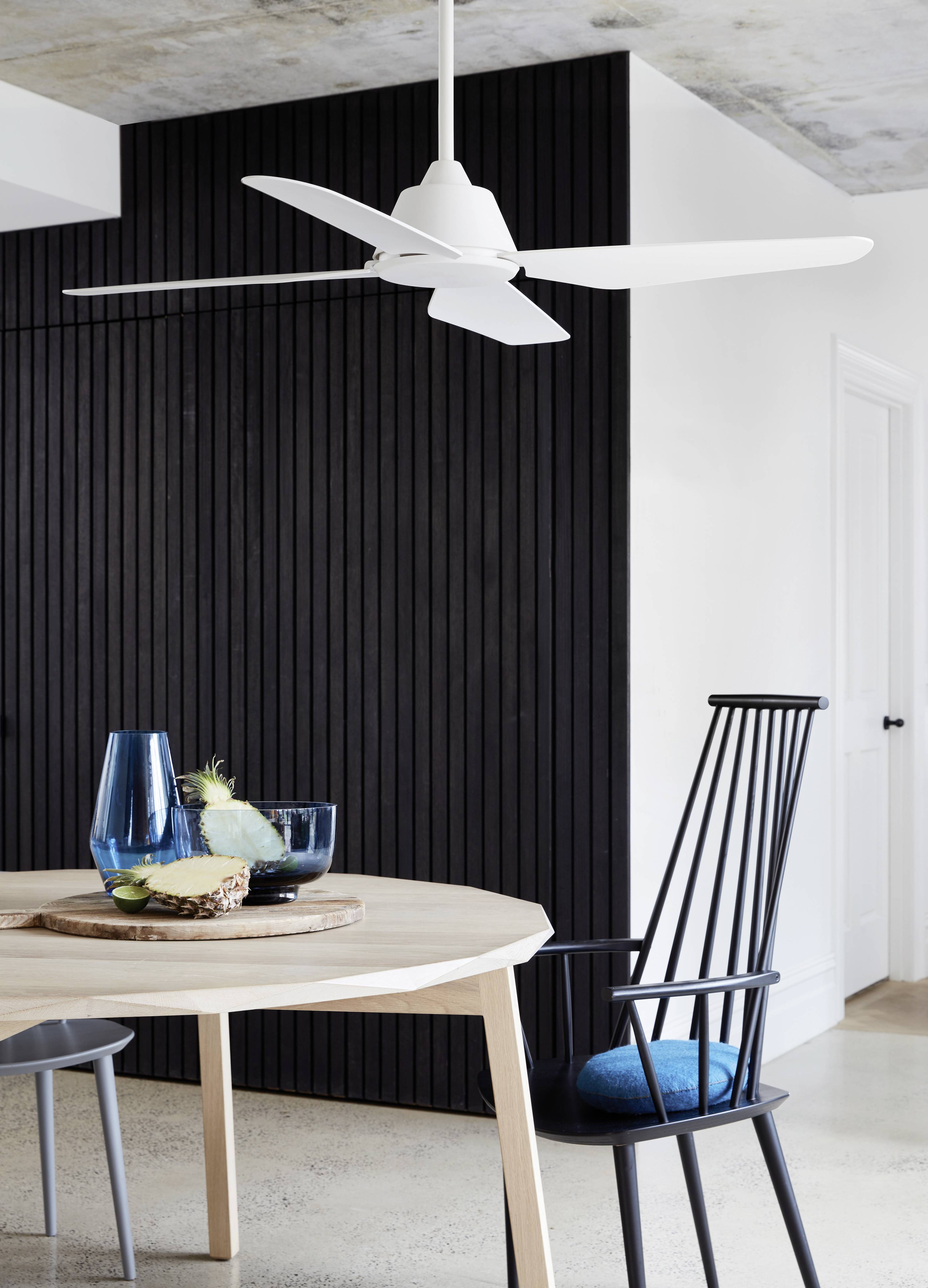 Dining room with a light wooden table, black chair and blue cushion. A tray with blue glasses and a pineapple sits on the table.