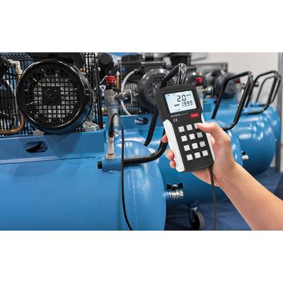 A hand is holding a measuring device in front of a blue air compressor. The screen displays '2.0', indicating the pressure.