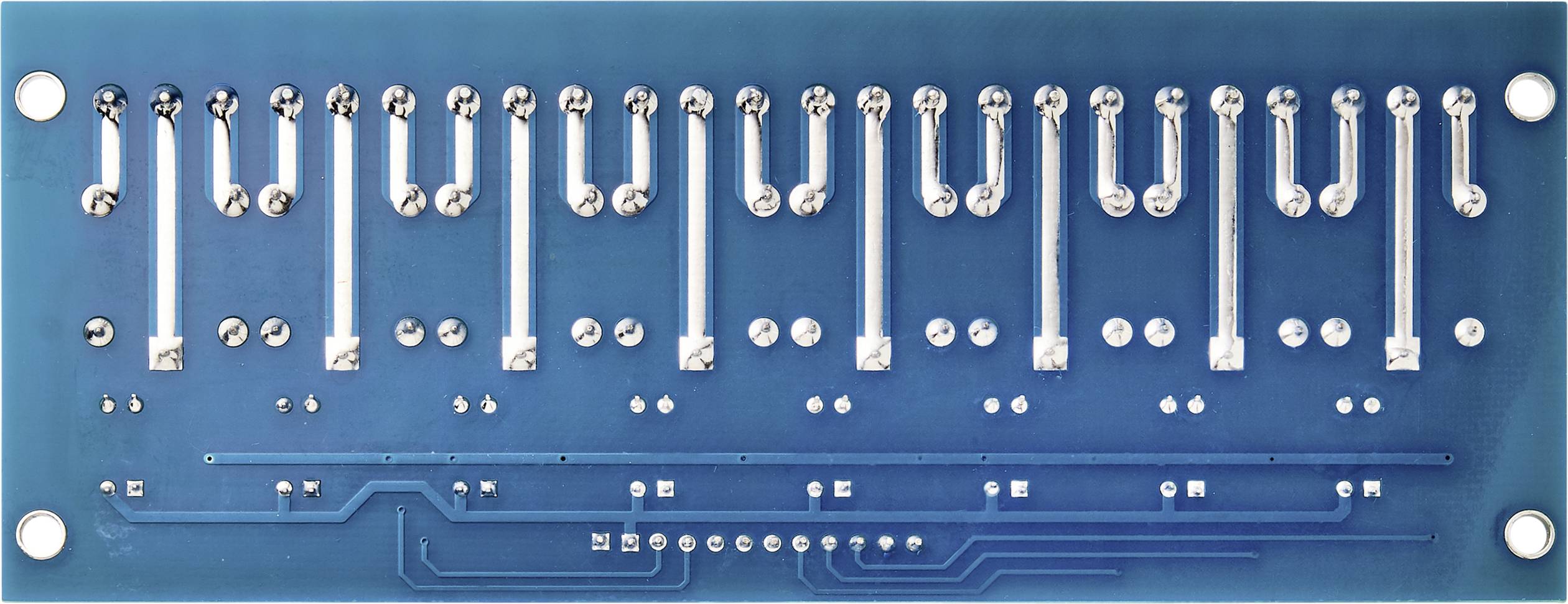 'Underside of a blue printed circuit board with soldered connections and circuit traces. Silver metallic contacts are visible.'
