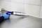 A person is applying sealant to the edge between a stainless steel surface and a tiled wall using a cartridge gun.