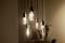 Several hanging light bulbs illuminate a dark room, creating a warm, cosy atmosphere. In the background, a blurred area with plants can be seen.